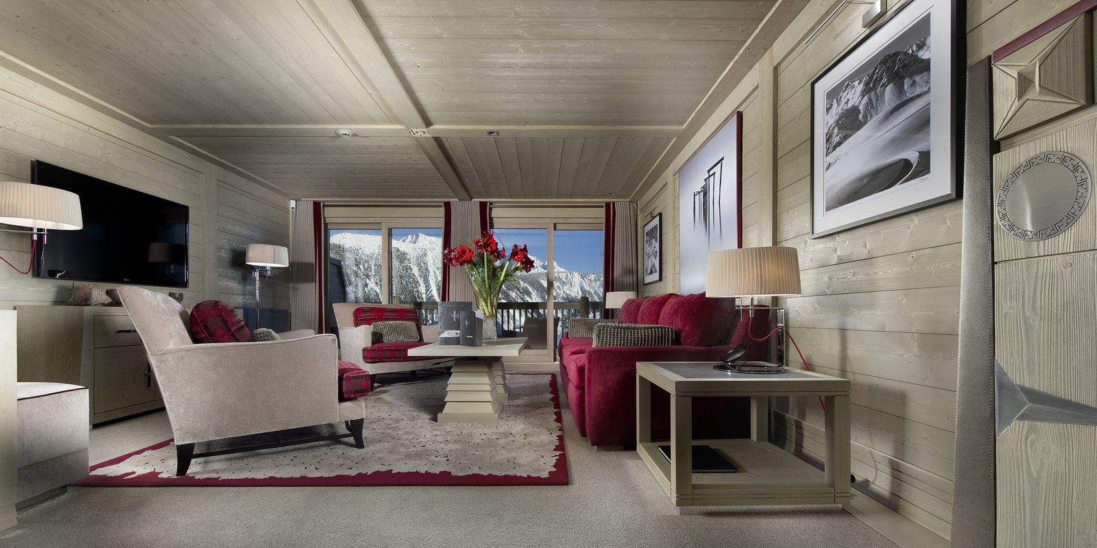 Hotel Le K2 Palace Courchevel Les 3 Vallees Frankrijk wintersport skivakantie luxe Suite living rde bank fauteuils TV salontafel bloemen vloerkleed grote ramen houten plafond uitzicht besneeuwde bergen sneeuw
