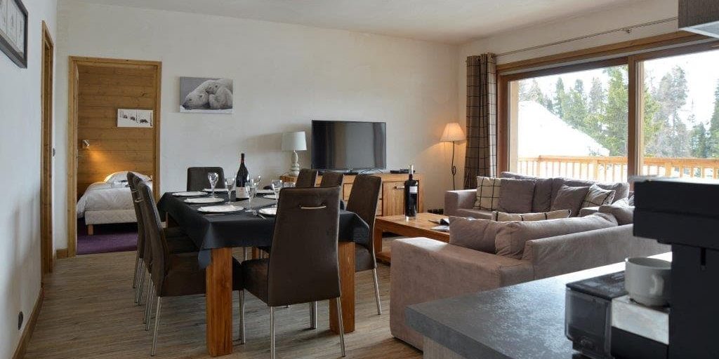 Residence Carlina Belle Plagne Paradiski Frankrijk wintersport skivakantie luxe appartement living gedekte tafel wijn wijnglazen stoelen grijze banken salontafel TV keuken slaapkamer grote ramen balkon bomen sneeuw