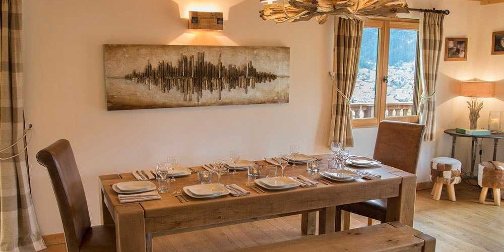 Chalet Belle Vache Chatel Les Portes du Soleil Frankrijk wintersport skivakantie luxe living gedekte tafel wijnglazen stoelen bankje schilderijen wandlamp kroonluchter hockers tafel raam bomen