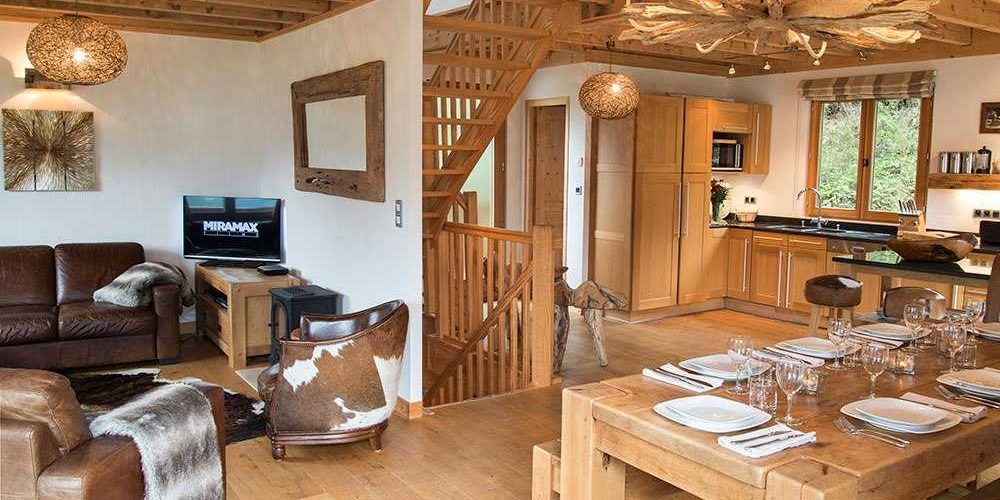 Chalet Belle Vache Chatel Les Portes du Soleil Frankrijk wintersport skivakantie luxe living bruine leren bank fauteuils TV hanglamp vloerkleed gedekte tafel keuken barkrukken kroonluchter trap hout