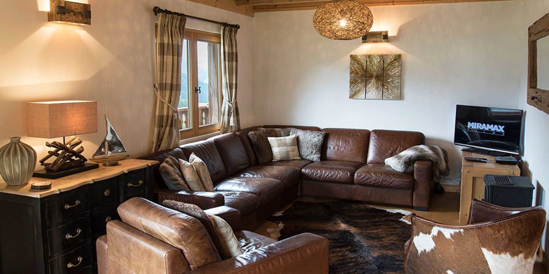 Chalet Belle Vache Chatel Les Portes du Soleil Frankrijk wintersport skivakantie luxe living bruine leren hoekbank fauteuils TV kastje lamp bootje vaas hanglamp schilderij spiegel raam balkon bergen