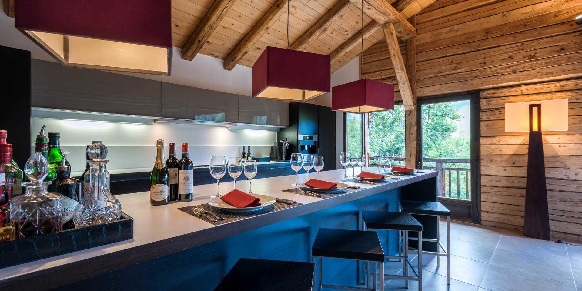 Chalet Ferme de Moudon Les Gets Les Portes du Soleil Frankrijk wintersport skivakantie luxe keuken bar barkrukken hanglampen wijn Champagne glazen Cognac likeur raam balkon houten wanden houten balken bomen
