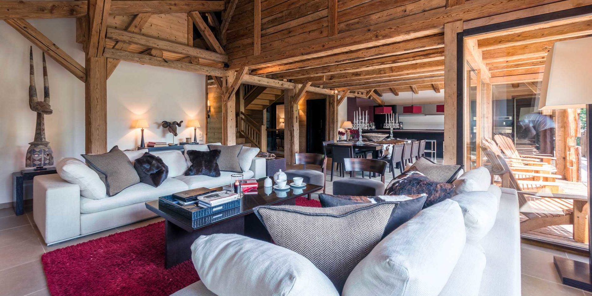 Chalet Ferme de Moudon Les Gets Les Portes du Soleil Frankrijk wintersport skivakantie luxe living witte banken kussens salontafel high tea kaars boeken rood vloerkleed eetkamer kandelaars rode hanglampen balkon ligstoelen houten balken