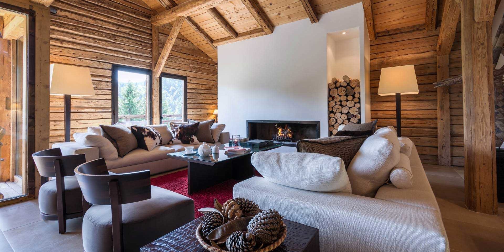 Chalet Ferme de Moudon Les Gets Les Portes du Soleil Frankrijk wintersport skivakantie luxe living open haard witte banken kussens fauteuils salontafel high tea dennenappels hout lamp raam houten wanden houten balken