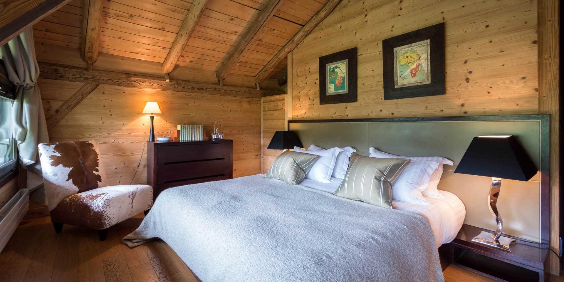 Chalet Ferme de Moudon Les Gets Les Portes du Soleil Frankrijk wintersport skivakantie luxe slaapkamer 2-persoonsbed witte sprei fauteuil schilderijen nachtlampjes houten wanden houten balken