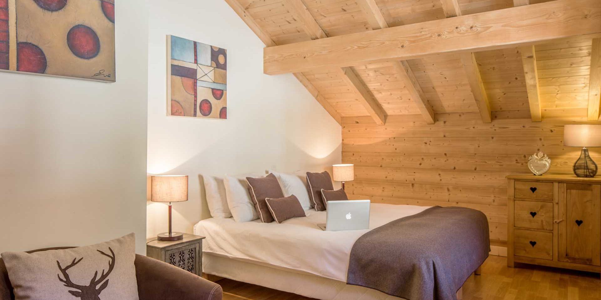 Chalet Grand Coeur Chatel Les Portes du Soleil Frankrijk wintersport skivakantie luxe slaapkamer 2-persoonsbed laptop sprei witte bruine kussens schilderijen fauteuil kussen gewei kastje houten balken