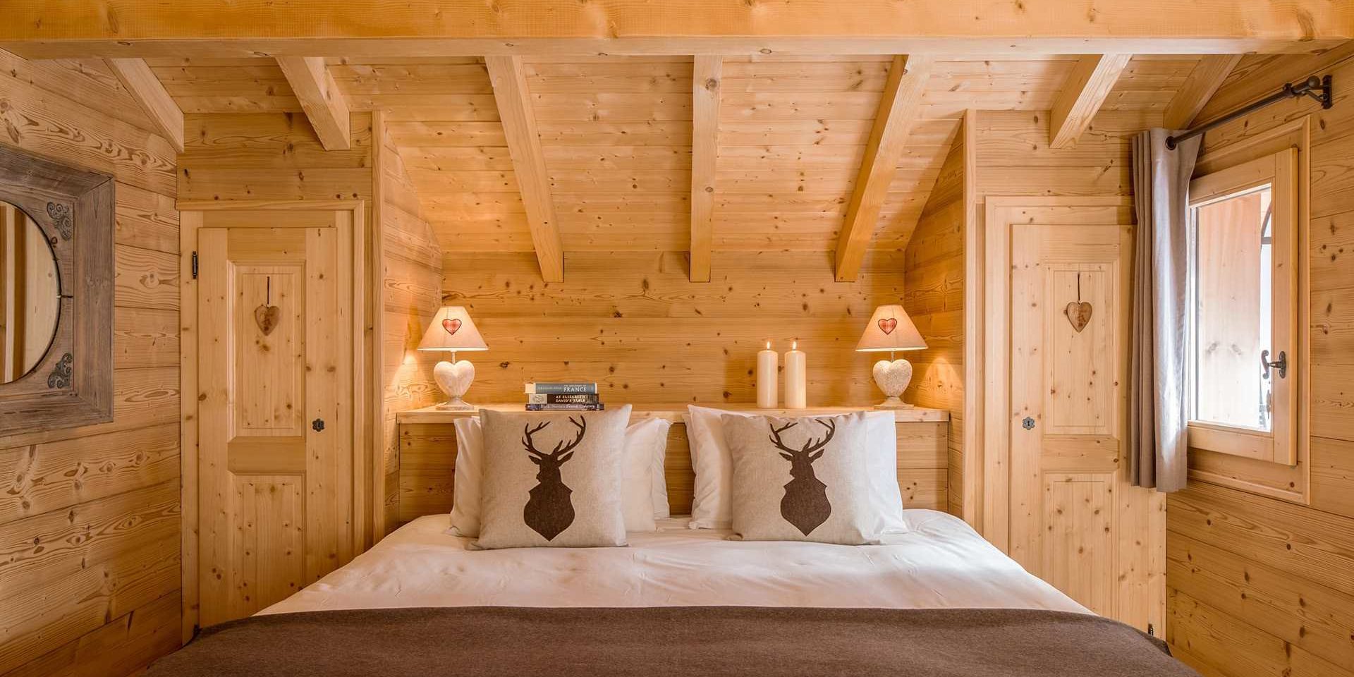 Chalet Grand Coeur Chatel Les Portes du Soleil Frankrijk wintersport skivakantie luxe slaapkamer 2-persoonsbed sprei witte kussens hert spiegel nachtlampjes kasten hartjes raam houten wanden houten balken