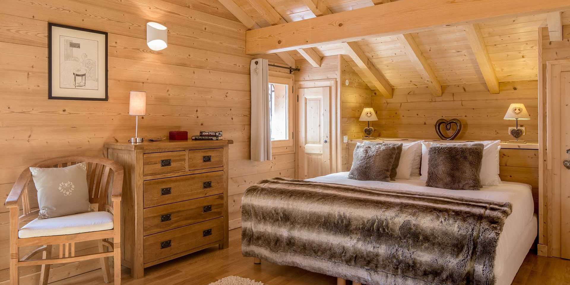 Chalet Grand Coeur Chatel Les Portes du Soleil Frankrijk wintersport skivakantie luxe slaapkamer 2-persoonsbed sprei witte bruine kussens nachtlampjes hartjes kast stoel schilderij vloerkleed houten wanden houten balken raam