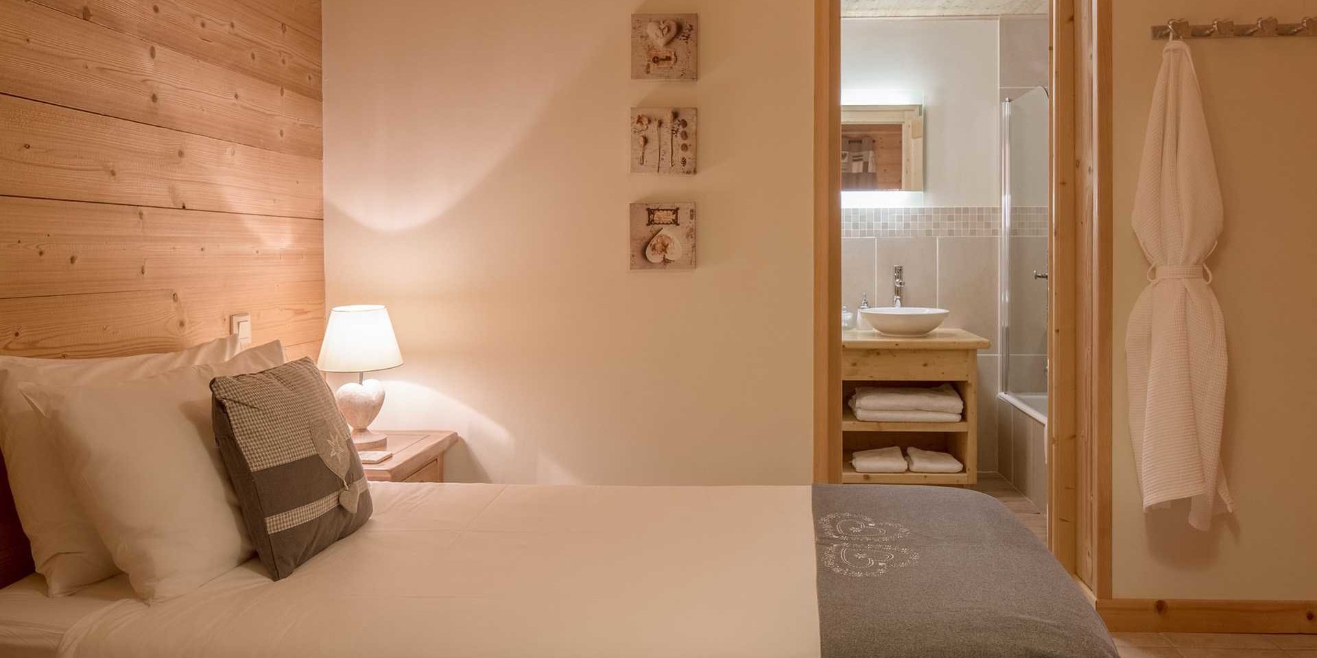 Chalet Grand Coeur Chatel Les Portes du Soleil Frankrijk wintersport skivakantie luxe slaapkamer 2-persoonsbed sprei witte grijze kussens nachtlampje schilderijen badjas kapstok badkamer bad wastafel spiegel handdoeken houten wand