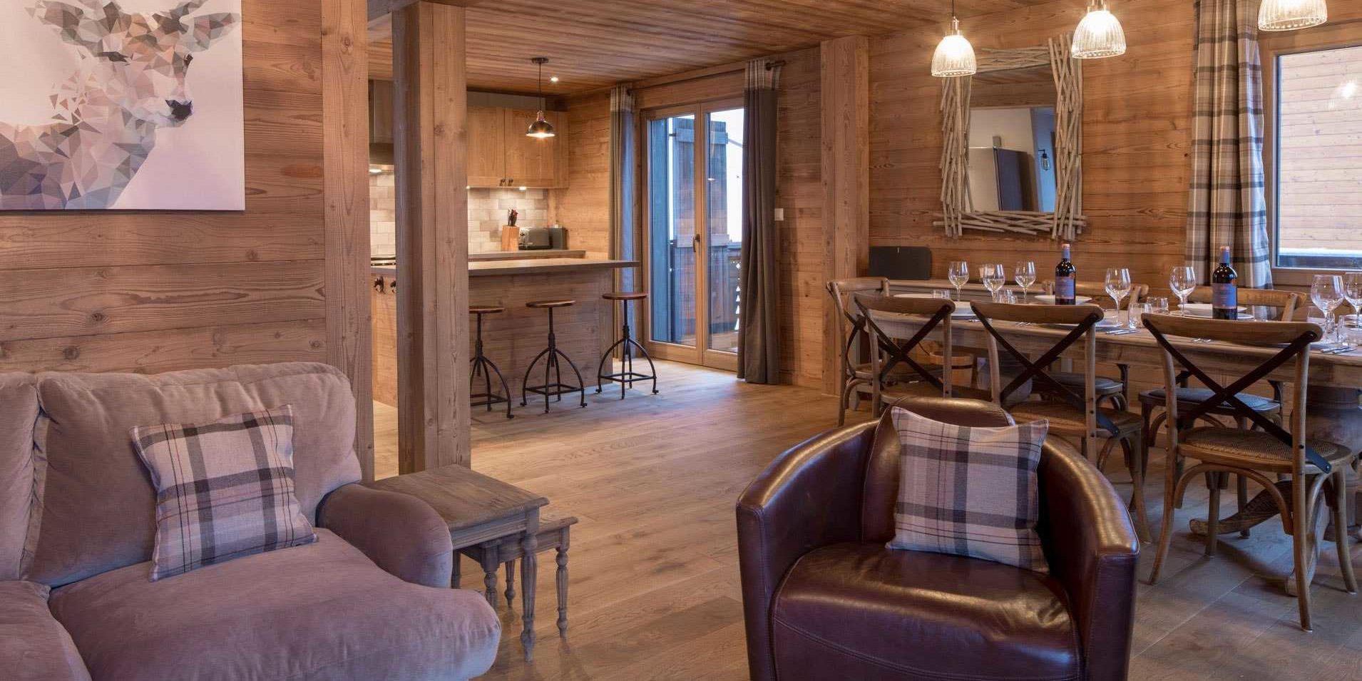 Chalet Les Clarines Chatel Les Portes du Soleil Frankrijk wintersport skivakantie luxe living loungebank bruine fauteuil gedekte tafel wijn wijnglazen houten stoelen hanglampen bar barkrukken schilderij hert spiegel raam balkon