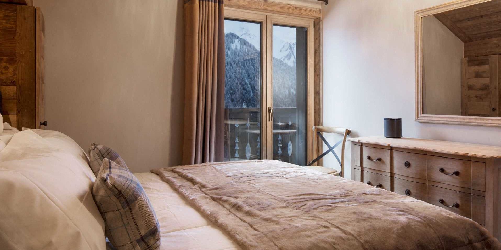 Chalet Les Clarines Chatel Les Portes du Soleil Frankrijk wintersport skivakantie luxe slaapkamer 2-persoonsbed sprei dressoir spiegel stoel raam balkon besneeuwde bergen bomen sneeuw