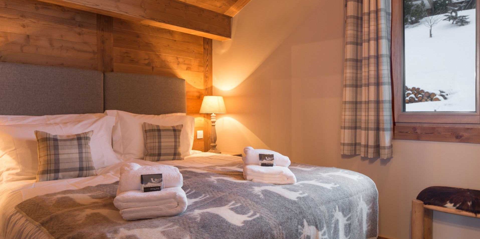 Chalet Les Clarines Chatel Les Portes du Soleil Frankrijk wintersport skivakantie luxe slaapkamer 2-persoonsbed sprei herten grijs hoofdbord kussens nachtlampjes handdoeken houten balken raam hout bomen sneeuw
