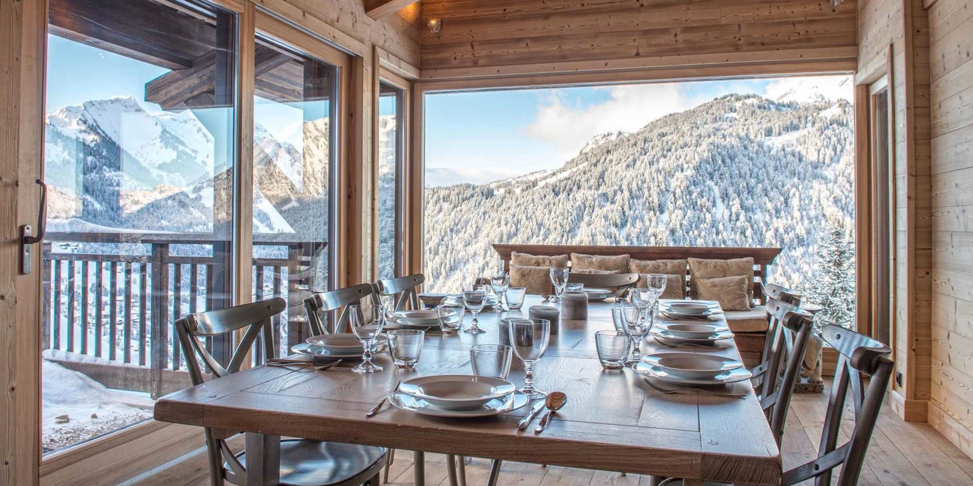 Chaletneuf du Tenne Chatel Les Portes du Soleil Frankrijk wintersport skivakantie luxe eetkamer gedekte tafel houten stoelen bank kussens grote ramen bomen bergen houten wanden balkon sneeuw