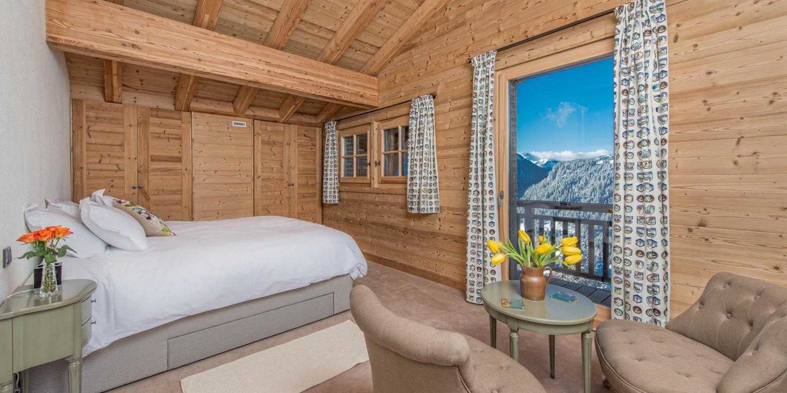 Chaletneuf du Tenne Chatel Les Portes du Soleil Frankrijk wintersport skivakantie luxe slaapkamer 2-persoonsbed groen nachtkastje bruine fauteuils tafeltje gele tulpen hoog raam uitzicht bergen bomen sneeuw houten wanden houten balken