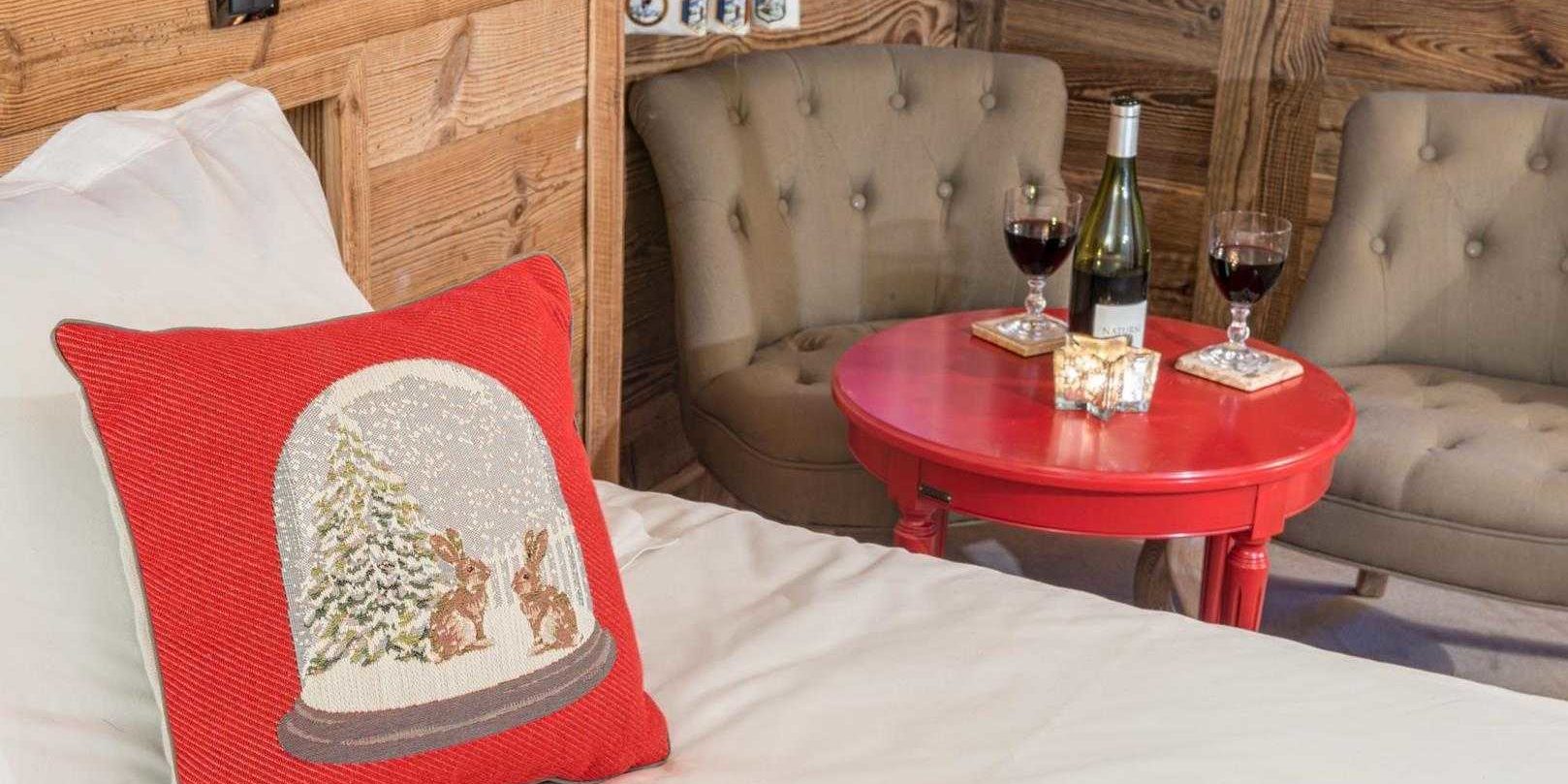 Chaletneuf du Tenne Chatel Les Portes du Soleil Frankrijk wintersport skivakantie luxe slaapkamer 2-persoonsbed rood kussen rood tafeltje wijn wijnglazen bruine fauteuils vloerkleed houten wanden