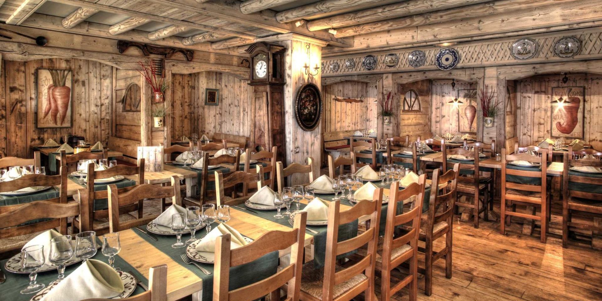 Hotel Village Montana Tignes Tignes-Val d'Isere Frankrijk wintersport skivakantie luxe restaurant La Chaumiere gedekte tafels wijnglazen schilderijen klok veel hout houten wanden houten plafond houten balken