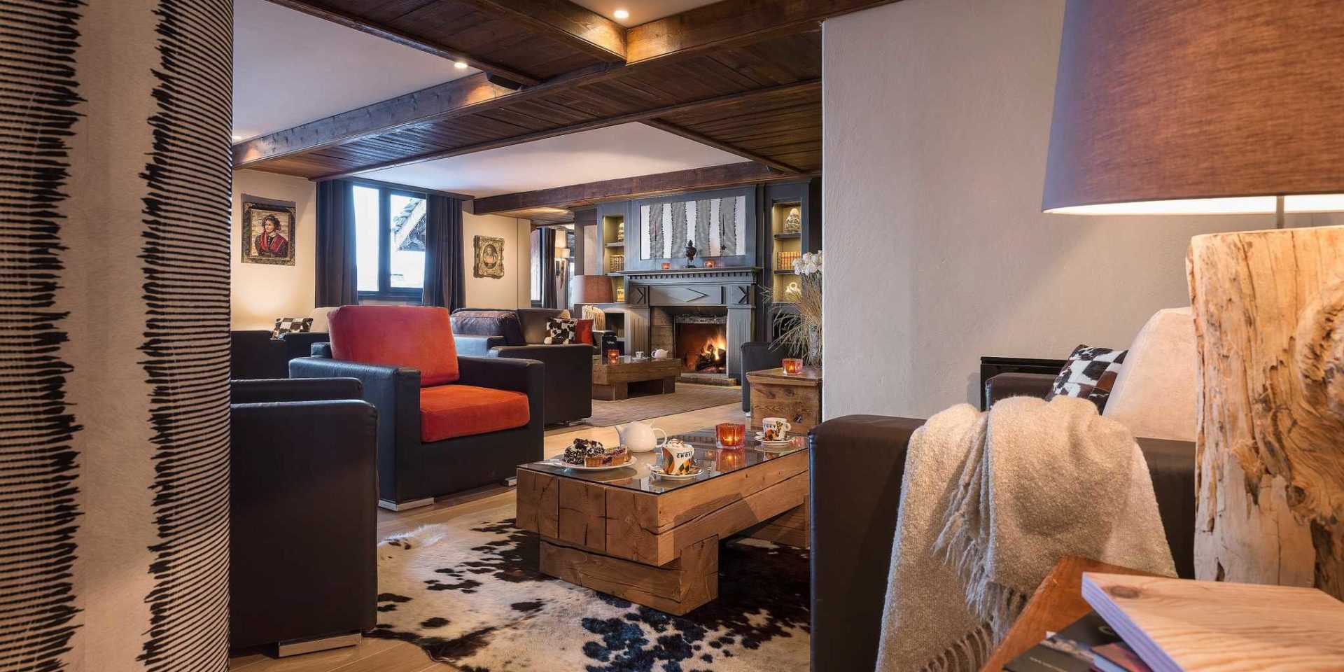 Hotel Village Montana Tignes Tignes-Val d'Isere Frankrijk wintersport skivakantie luxe lounge zwarte fauteuils rode kussens wit kleed lampen salontafel high tea kaarsen houten balken schilderijen open haard vloerkleed