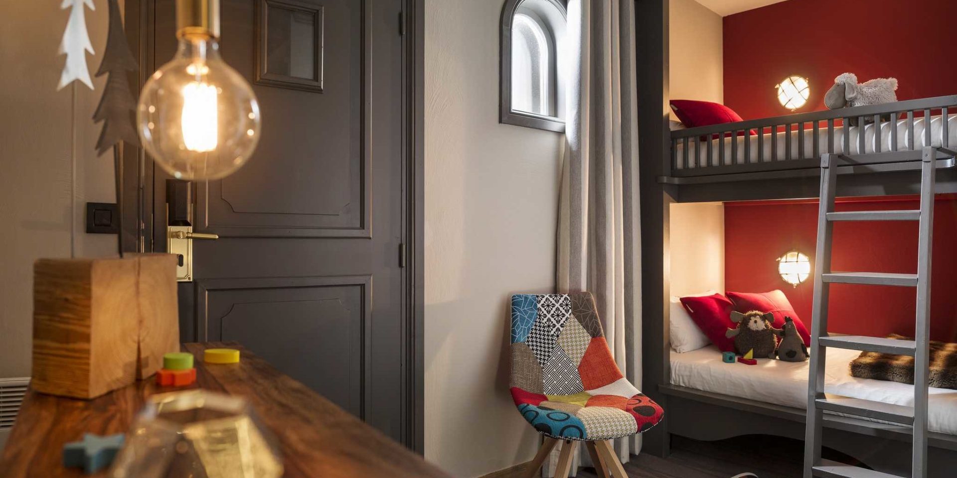 Hotel Village Montana Tignes Tignes-Val d'Isere Frankrijk wintersport skivakantie luxe slaapkamer stapelbed rode muur rode kussens knuffels speelgoed kinderkamer gekleurde stoel lamp trap