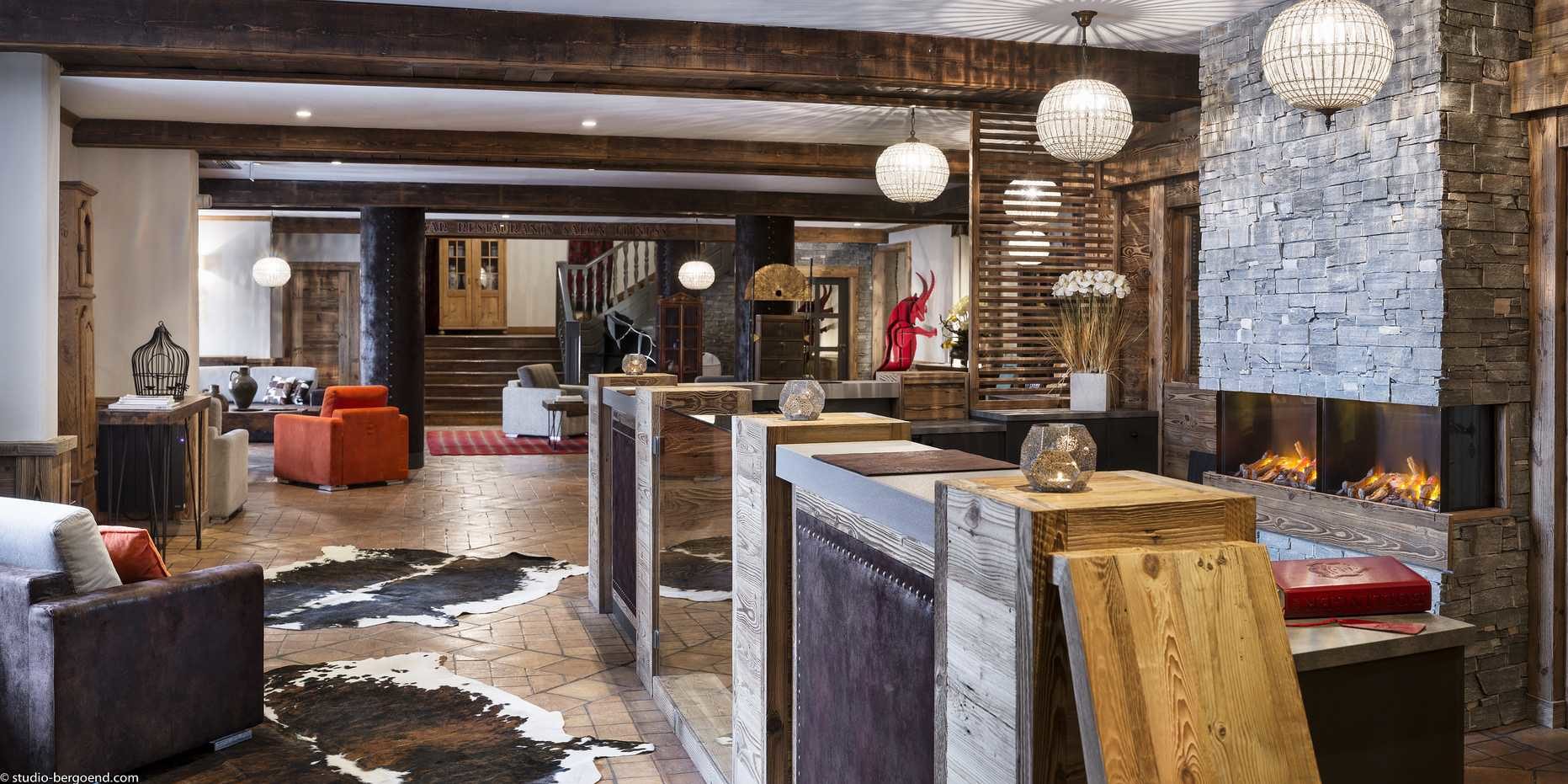 Hotel Village Montana Tignes Tignes-Val d'Isere Frankrijk wintersport skivakantie luxe lounge open haard stenen muur oranje bruine fauteuils vloerkleden hanglampen trap houten balken