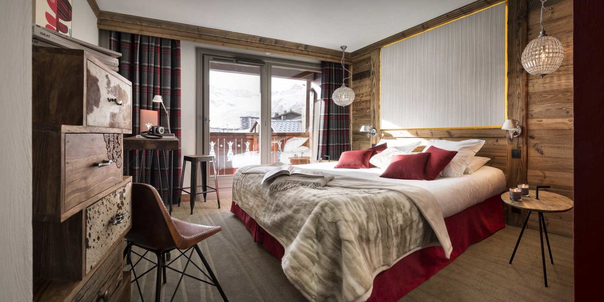 Hotel Village Montana Tignes Tignes-Val d'Isere Frankrijk wintersport skivakantie luxe slaapkamer 2-persoonsbed rode kussens sprei handlamp tafeltje bruine stoel kast geblokte gordijnen balkon bergen