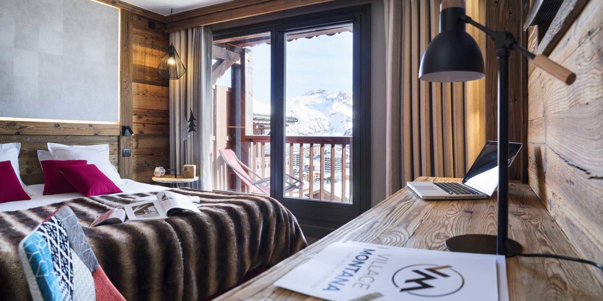 Hotel Village Montana Tignes Tignes-Val d'Isere Frankrijk wintersport skivakantie luxe slaapkamer 2-persoonsbed roze kussens sprei boeken gekleurde stoel bureau bureaulamp raam balkon ligstoel besneeuwde bergen