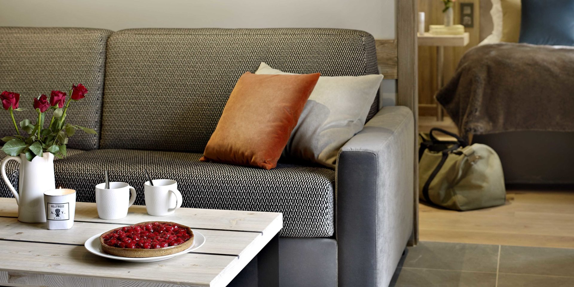 MGM Residence Les Chalets Elena Les Houches Chamonix Mont Blanc Frankrijk wintersport skivakantie luxe living grijze bank salontafel rode rozen thee taart oranje grijze kussens tas slaapkamer