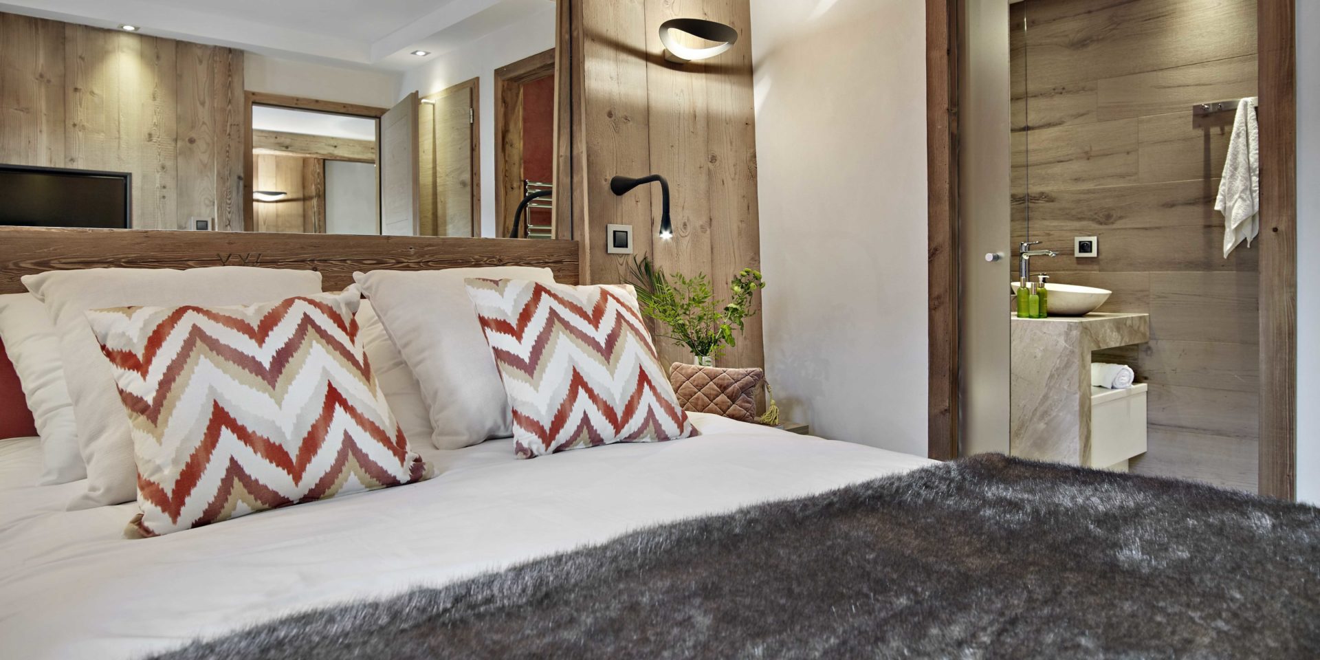 MGM Residence Alexane Samoens Le Grand Massif Frankrijk wintersport skivakantie luxe slaapkamer 2-persoonsbed rood witte kussens grote spiegel sprei plant wandlampjes badkamer wastafel handdoek houten wand