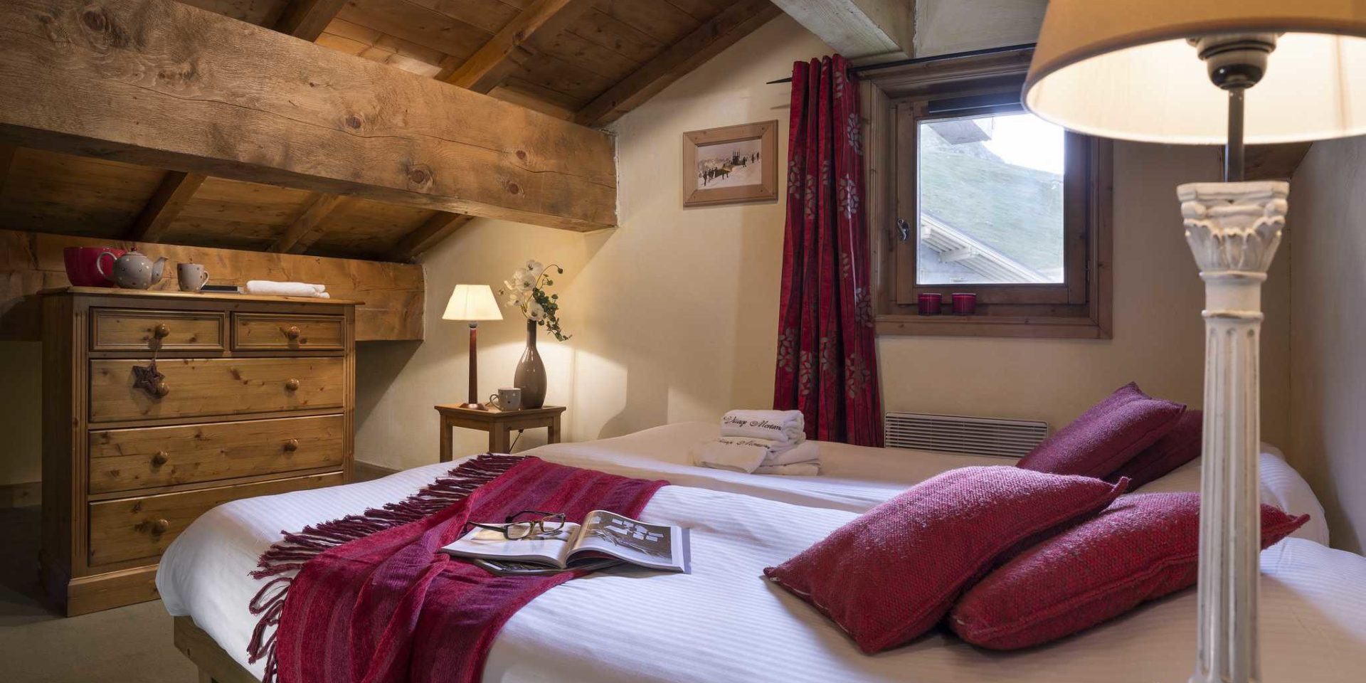 Residences Village Montana Tignes Tignes-Val d'Isere Frankrijk wintersport skivakantie luxe slaapkamer aparte bedden kleed rode kussens kast nachtlampje theepot schilderij raam rood gordijn rode kaarsen houten balken bomen