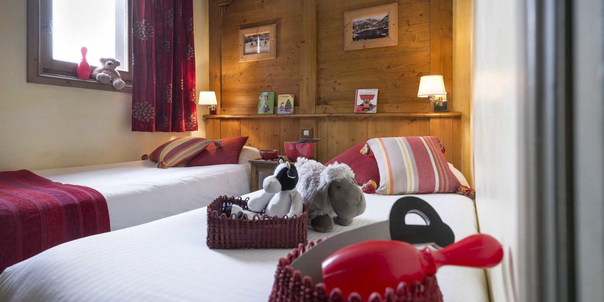 Residences Village Montana Tignes Tignes-Val d'Isere Frankrijk wintersport skivakantie luxe slaapkamer aparte bedden rode gestreepte kussens knuffels speelgoed beer boekjes houten wand schilderijen wandlampjes