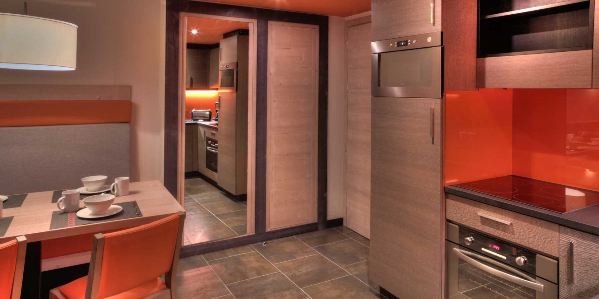 Residence Montana Plein Sud Val Thorens Les 3 Vallees Frankrijk wintersport skivakantie luxe living 4K6 gedekte tafel oranje stoelen bankje hanglamp keuken houten wanden oranje wand