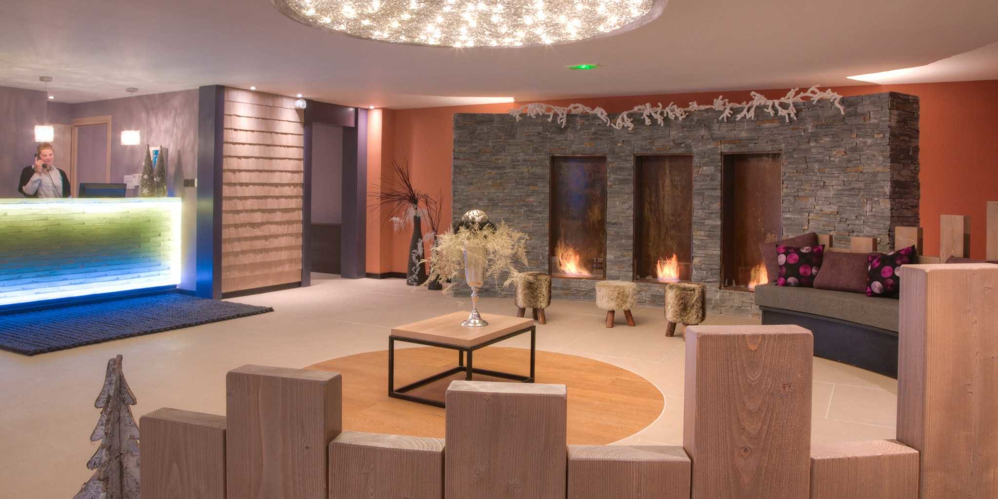 Residence Montana Plein Sud Val Thorens Les 3 Vallees Frankrijk wintersport skivakantie luxe receptie receptioniste hanglamp houten border ronde bank kussens open haard hockers planten oranje muur