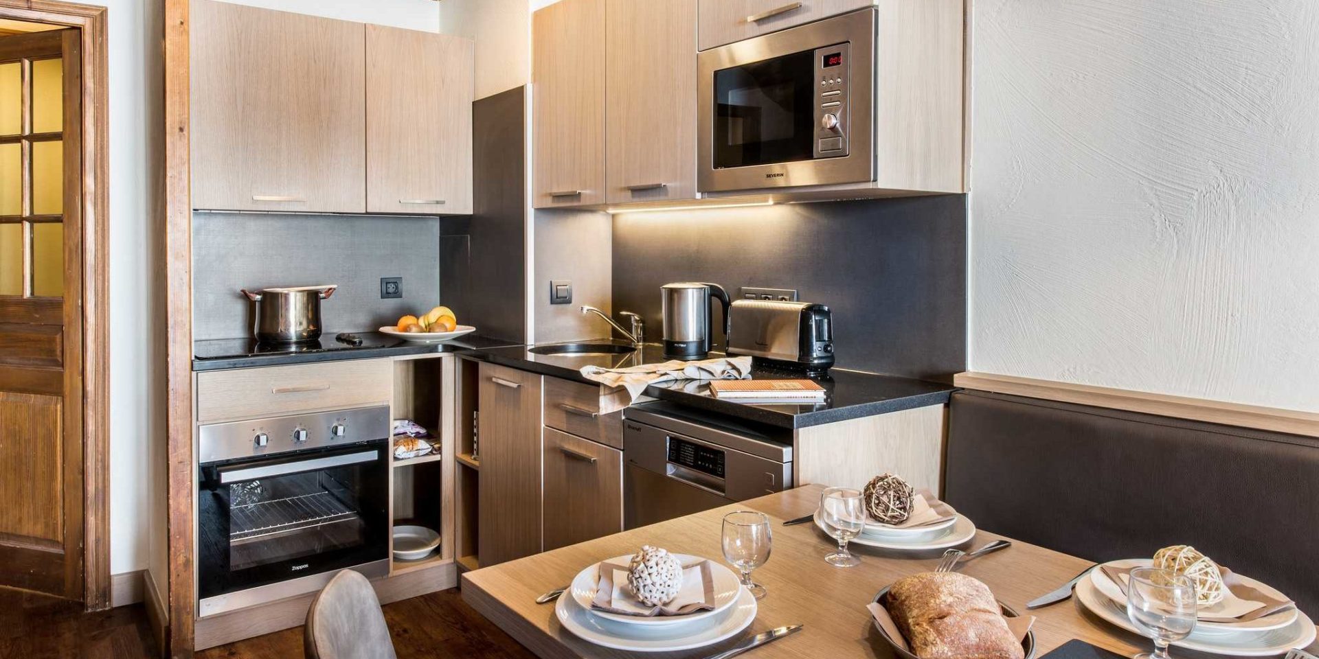 Residences Village Montana Val Thorens Les 3 Vallees Frankrijk wintersport skivakantie luxe keuken 4K6 66m2 gedekte tafel brood bankje stoelen houten kastjes vers fruit pan waterkoker