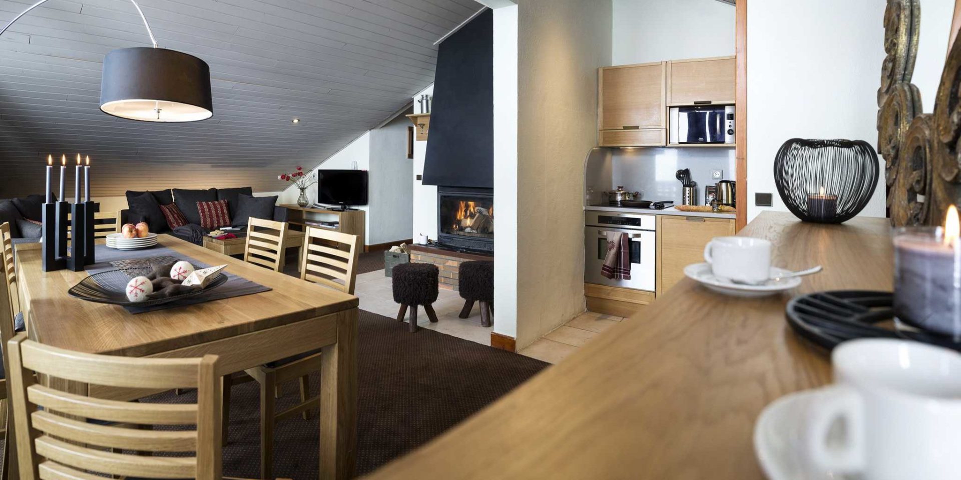 Residences Village Montana Val Thorens Les 3 Vallees Frankrijk wintersport skivakantie luxe living 4K6 open haard eettafel kaarsen vers fruit houten stoelen hanglamp vloerkleed hockers bank TV bloemen keuken koffiekopjes kaars