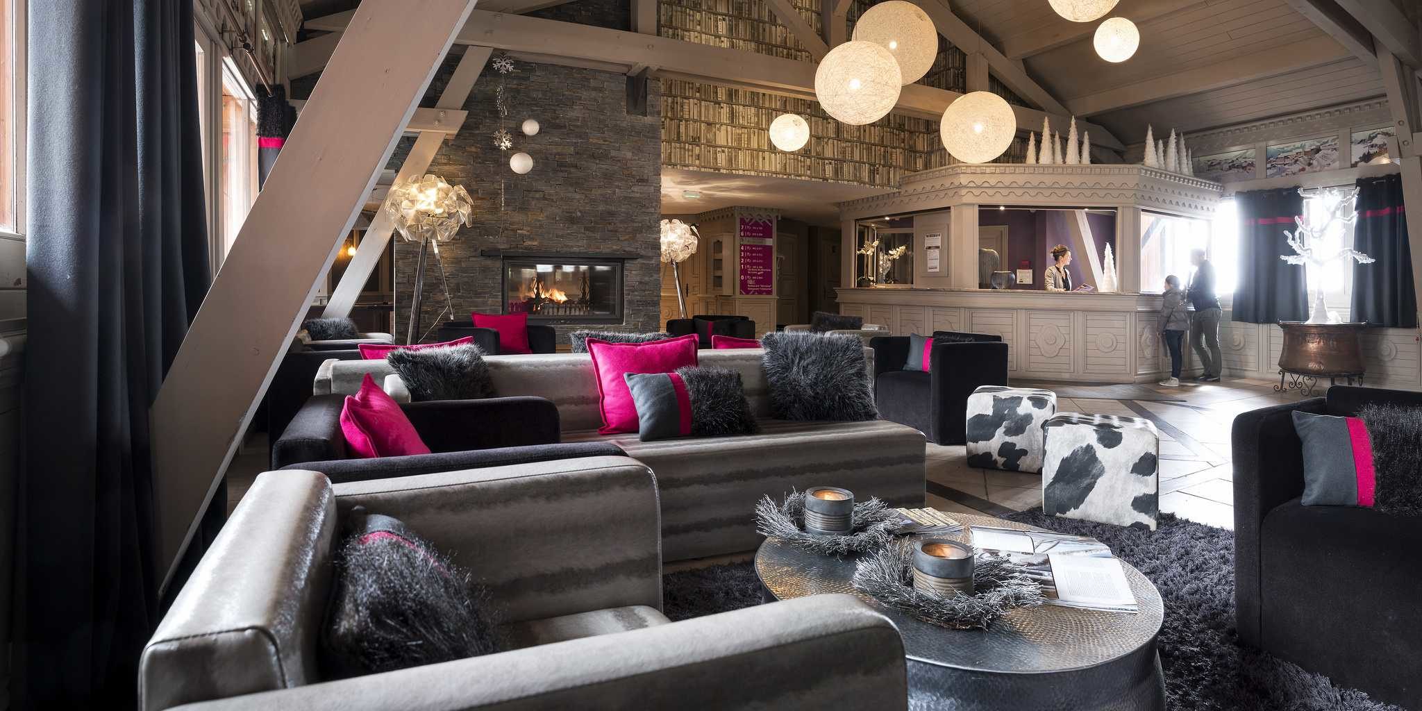 Residences Village Montana Val Thorens Les 3 Vallees Frankrijk wintersport skivakantie luxe lounge receptie grijze bank zwart roze kussens fauteuils salontafel kaarsen hockers vloerkleed hanglampen houten balken open haard