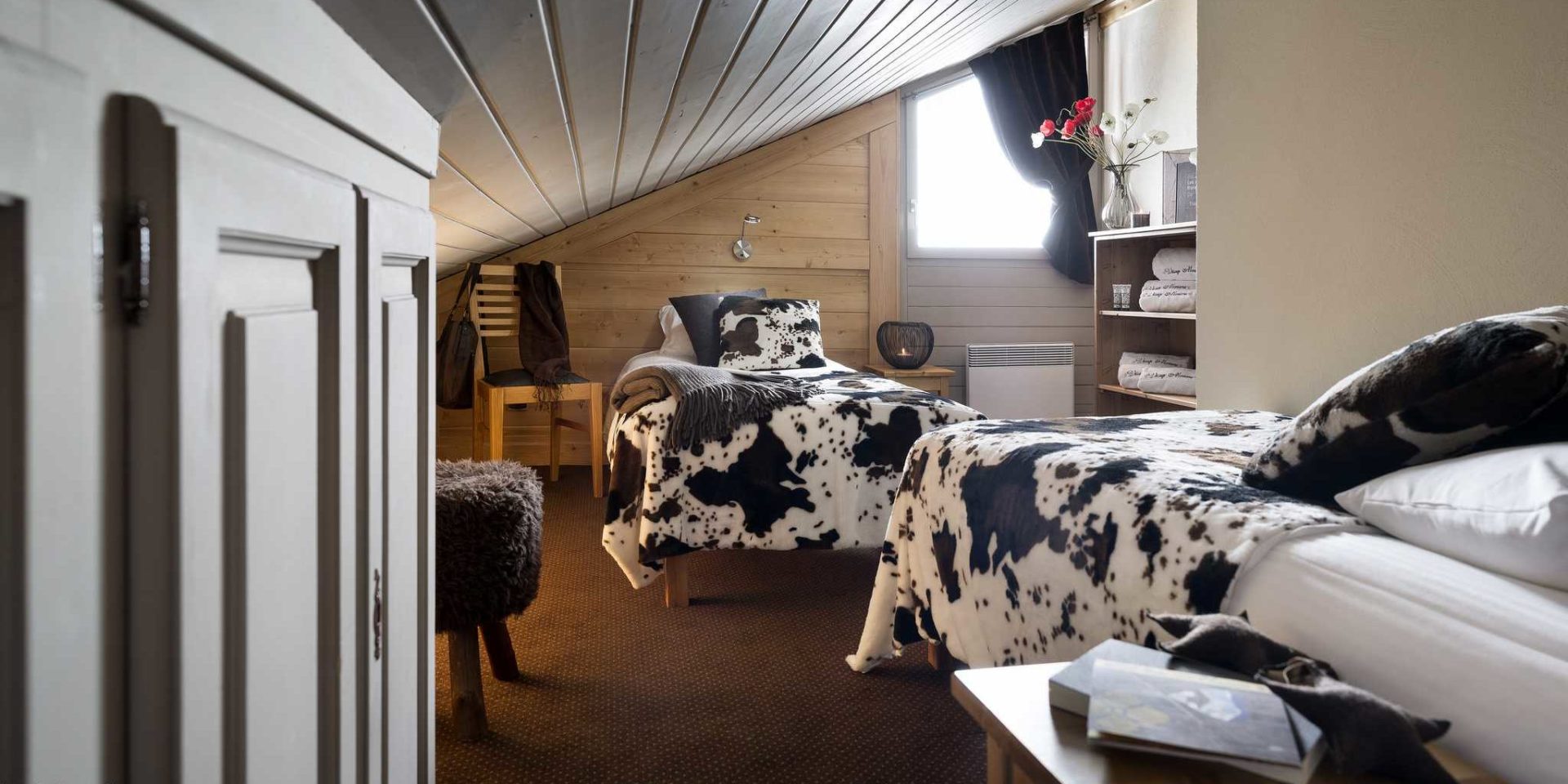 Residences Village Montana Val Thorens Les 3 Vallees Frankrijk wintersport skivakantie luxe slaapkamer aparte bedden sprei koeienprint boeken stoel hocker handdoeken bloemen houten wanden houten plafond vloerbedekking