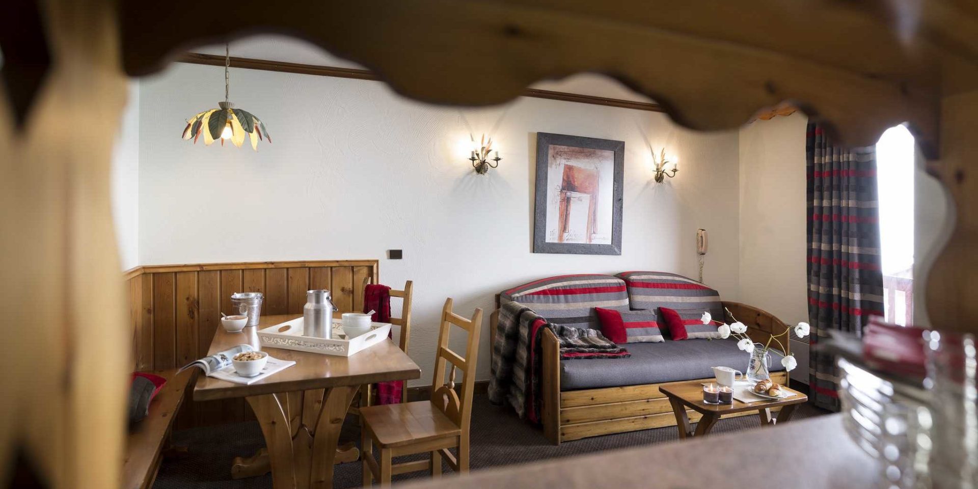 Residences Village Montana Val Thorens Les 3 Vallees Frankrijk wintersport skivakantie luxe living 3K4 gedekte tafel houten bankje houten stoelen hanglamp wandlampen schilderij bank gestreepte kussens salontafel bloemen kaarsen gestreepte gordijnen raam balkon