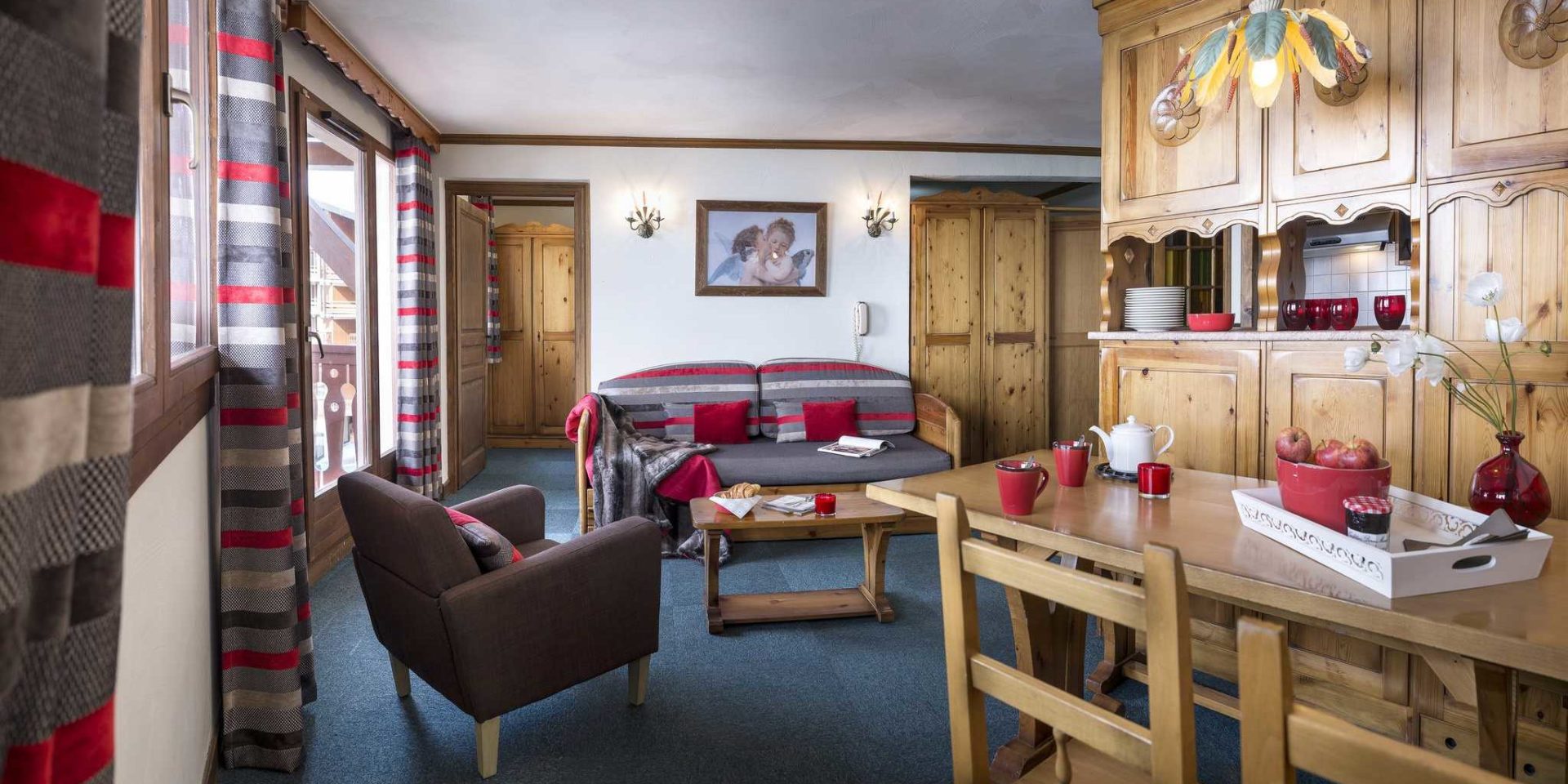 Residences Village Montana Val Thorens Les 3 Vallees Frankrijk wintersport skivakantie luxe living 3K6 eettafel theepot vers fruit vaas bloemen houten stoelen bank fauteuil salontafel kaars houten kastenwand raam gestreepte gordijnen