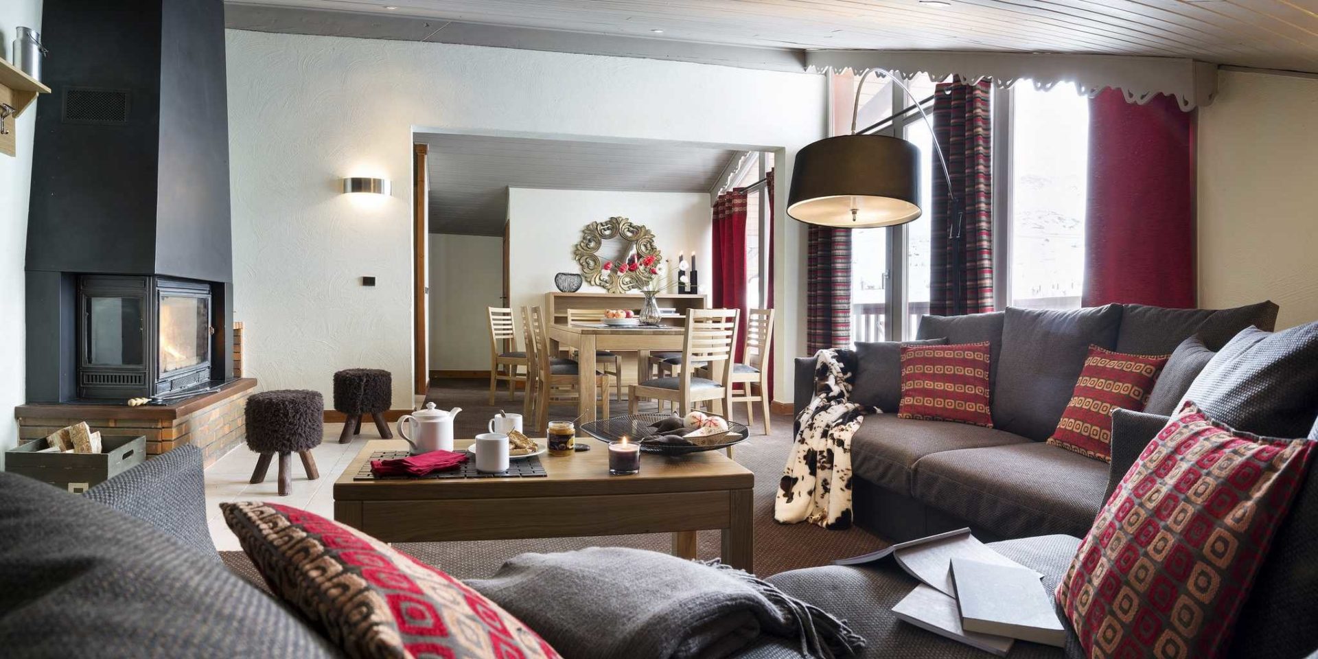 Residences Village Montana Val Thorens Les 3 Vallees Frankrijk wintersport skivakantie luxe living 4K6 open haard hockers grote grijze banken kussens salontafel theepot kaars hanglamp eettafel houten stoelen rode gordijnen spiegel