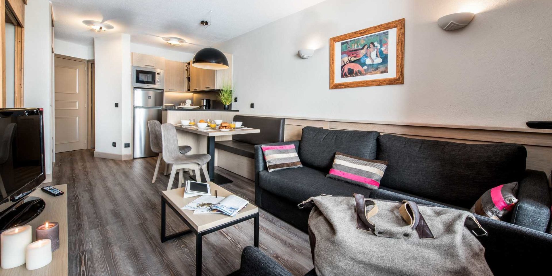 Residences Village Montana Val Thorens Les 3 Vallees Frankrijk wintersport skivakantie luxe living 2K4 grijze bank gestreepte kussens tas salontafel boeken TV kaarsen schilderij gedekte tafel broodjes hanglamp bankje stoelen keuken