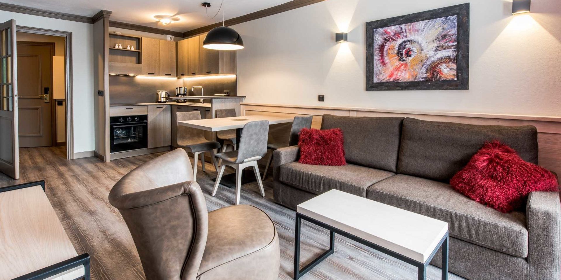 Residences Village Montana Val Thorens Les 3 Vallees Frankrijk wintersport skivakantie luxe living 3K4 grijze bank rode kussens fauteuil salontafel schilderij eettafel hanglamp stoelen keuken