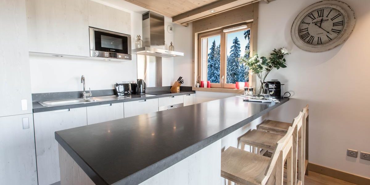 Alpine Residences Courchevel Les 3 Vallees Frankrijk wintersport skivakantie luxe Aspen Lodge keuken kookeiland barkrukken klok bloemen raam bomen