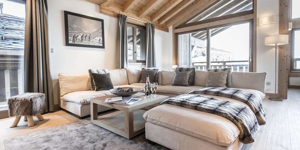 Alpine Residences Courchevel Les 3 Vallees Frankrijk wintersport skivakantie luxe Aspen Lodge living lounge hoekbank Champagne glazen hocker vloerkleed schilderij ramen houten balken