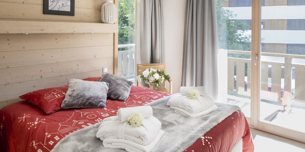 Alpine Residences Courchevel Les 3 Vallees Frankrijk wintersport skivakantie luxe Aspen Lodge slaapkamer 2-persoonsbed rode bedsprei handdoeken badjassen schilderij bloemen raam