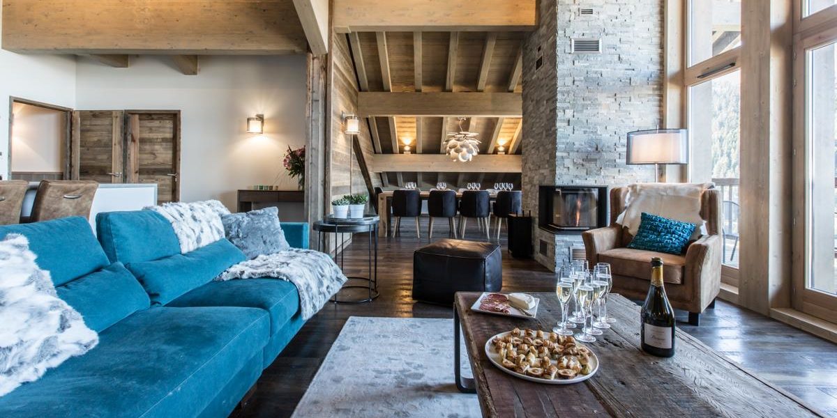 Alpine Residences Courchevel Les 3 Vallees Frankrijk wintersport skivakantie luxe Keystone Lodge blauwe bank vloerkleed hapjes Champagne fauteuil open haard eetkamer houten balken ramen