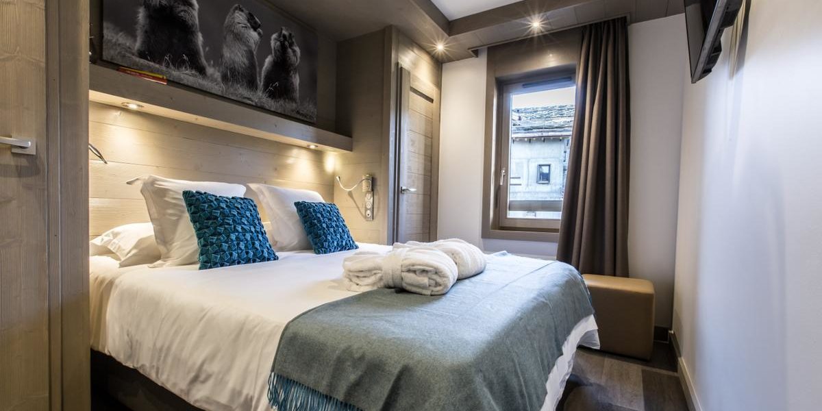 Alpine Residences Courchevel Les 3 Vallees Frankrijk wintersport skivakantie luxe Keystone Lodge slaapkamer 2-persoonsbed blauwe kussens badjassen schilderij marmotten raam