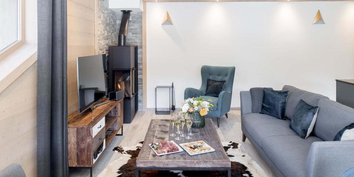 Alpine Residences Courchevel Les 3 Vallees Frankrijk wintersport skivakantie luxe Mammoth Lodge bank fauteuil Champagne hapjes vloerkleed bloemen houtkachel TV