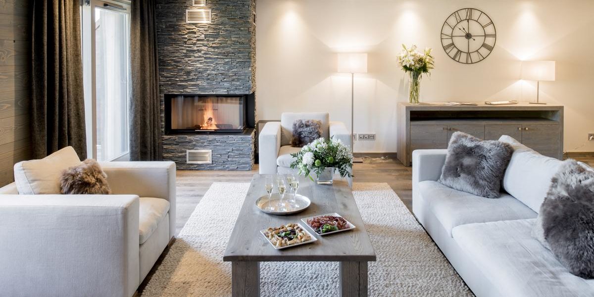 Alpine Residences Courchevel Les 3 Vallees Frankrijk wintersport skivakantie luxe Mammoth Lodge bank fauteuil vloerkleed Champagneglazen hapjes open haard klok kast bloemen
