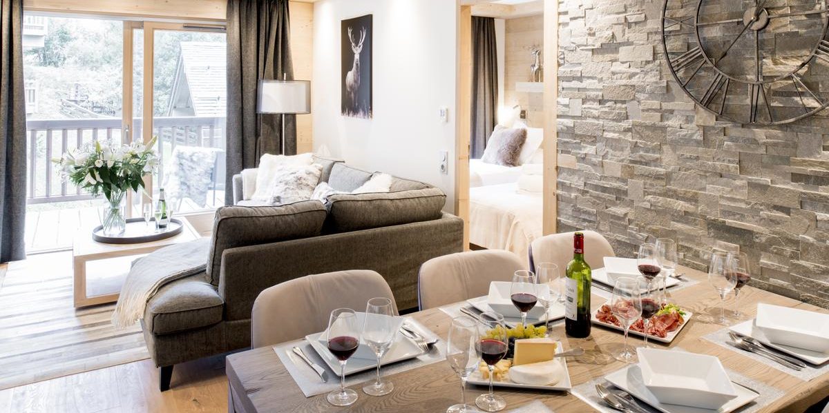 Alpine Residences Courchevel Les 3 Vallees Frankrijk wintersport skivakantie luxe Mammoth Lodge eetkamer gedekte tafel wijn wijnglazen fruit klok hoekbank bloemen schilderij raam balkon