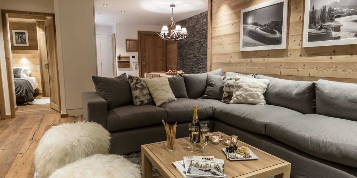 Alpine Residences Courchevel Les 3 Vallees Frankrijk wintersport skivakantie luxe Whistler Lodge lounge hoekbank Champagne hapjes kaarsen hockers vloerkleed schilderijen hanglamp hout