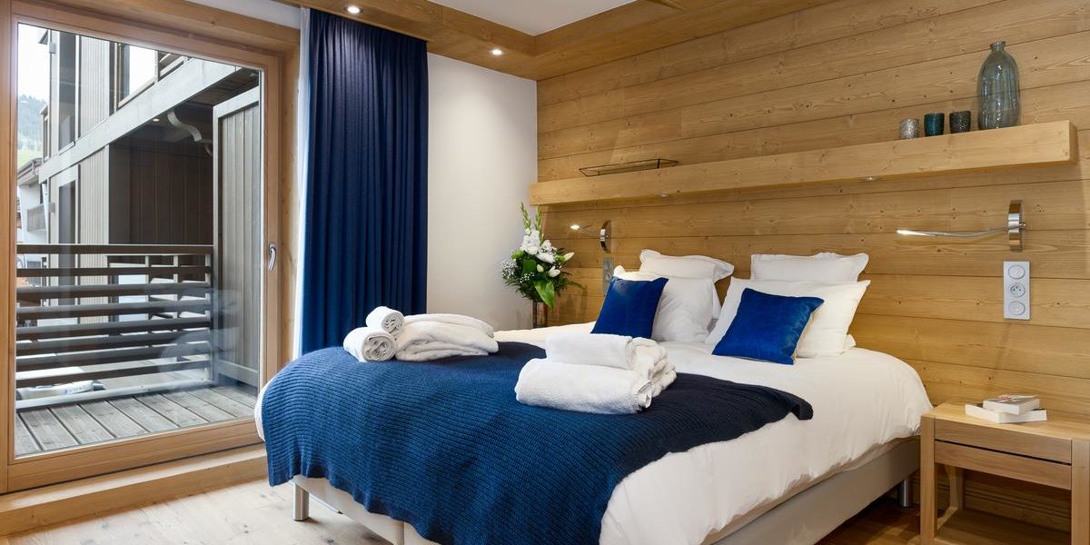 Alpine Residences Les Gets Les Portes du Soleil Frankrijk wintersport skivakantie luxe Annapurna slaapkamer 2-persoonsbed blauwe bedsprei handdoeken hout raam balkon